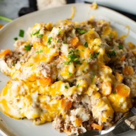 A photo of our low carb cheesy ground beef and cauliflower rice casserole on a white plate covered in melted cheese.