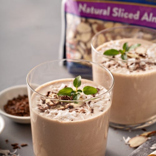 Two glasses of almond joy protein shakes, shaved chocolate, a package of Fisher's slivered almonds, coconut topped with mint leaves
