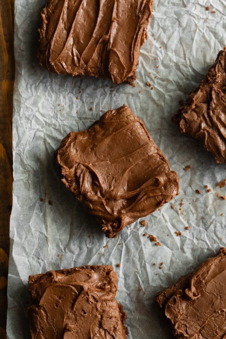 Thick, chocolate brownies with rich frosting cooling on parchment paper after baking.