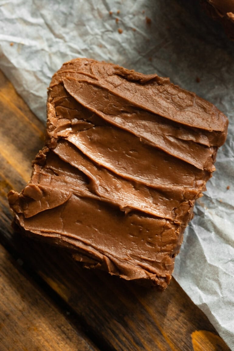 Homemade lunch lady brownies with a rustic layer of chocolate frosting, cut into squares on parchment.