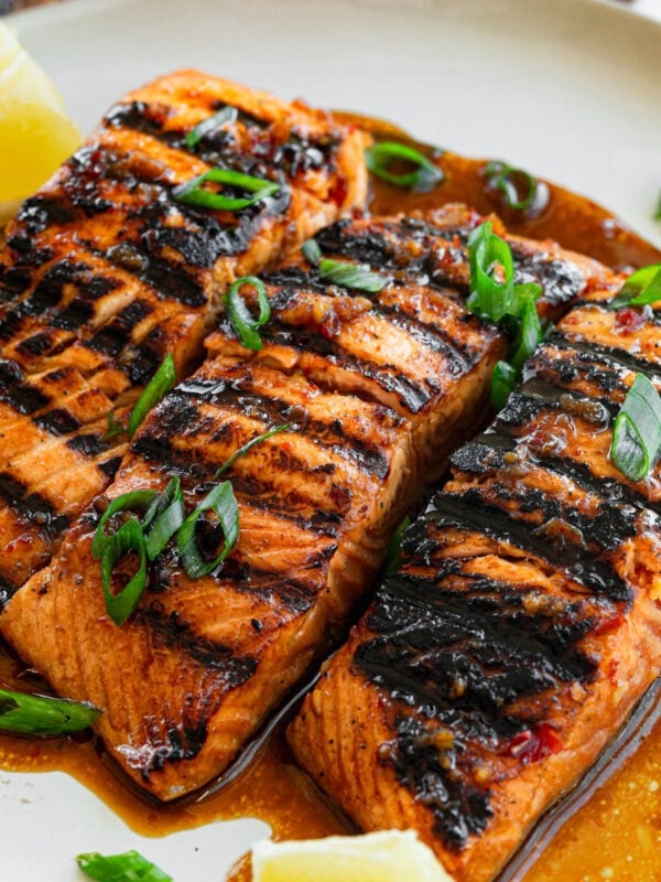 three grilled salmon filets sitting on a white plate sitting in a saucy marinade