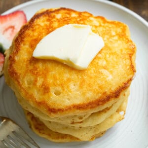 a photo of a stack of several golden fluffy buttermilk pancakes with a pat of butter on top