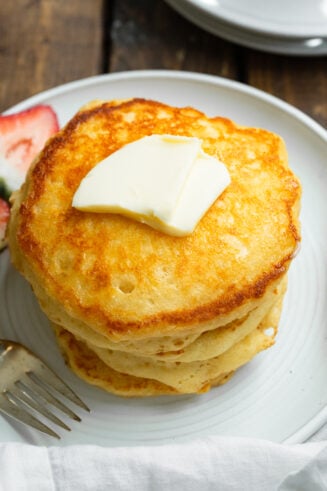 a photo of a stack of several golden fluffy buttermilk pancakes with a pat of butter on top