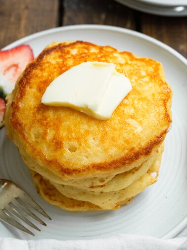 a photo of a stack of several golden fluffy buttermilk pancakes with a pat of butter on top