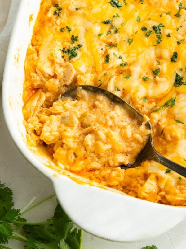 Mexican chicken and rice casserole topped with fresh chopped parsley and melted cheese with a spoon scooping up a serving