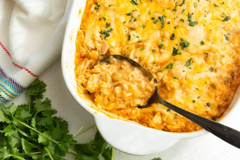 Mexican chicken and rice casserole topped with fresh chopped parsley and melted cheese with a spoon scooping up a serving