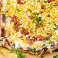 A photo of elote mexican corn grilled pizza with bacon and cilantro on top.