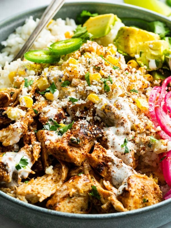 a mexican chicken rice bowl topped with creamy elote, picked red onions, avocado and jalapeno slices