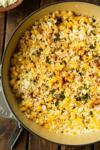 a photo of a dutch oven full of creamy mexican street corn topped with fresh cilantro and sprinkled chili powder