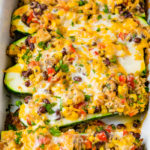 a casserole dish of cheesy healthy mexican zucchini boats with brown rice, peppers, beans, tomatoes, salsa and cheese