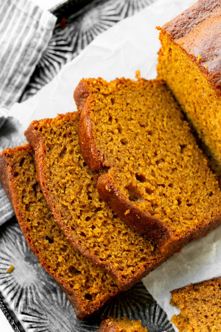 a photo of a loaf of pumpkin bread with three pieces sliced off the end and laying down next to the rest of the loaf.