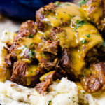 A photo of beef short ribs smothered in mustard Carolina BBQ sauce over a pile of mashed potatoes.