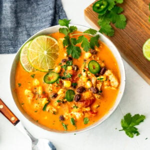a bowl of chicken enchilada soup topped with slices of lime, cilantro leaves, jalapeno slices, etc