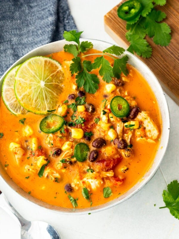 a bowl of chicken enchilada soup topped with slices of lime, cilantro leaves, jalapeno slices, etc
