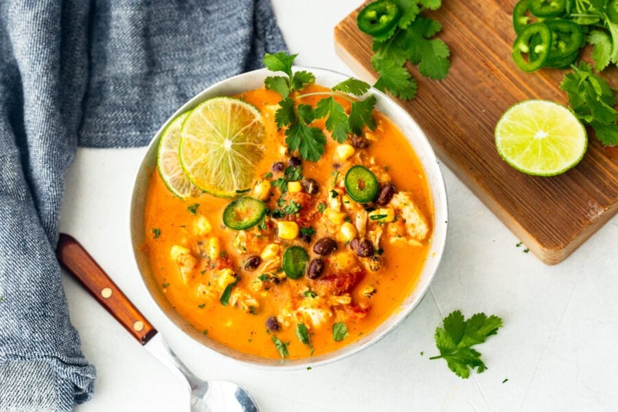 a bowl of chicken enchilada soup topped with slices of lime, cilantro leaves, jalapeno slices, etc