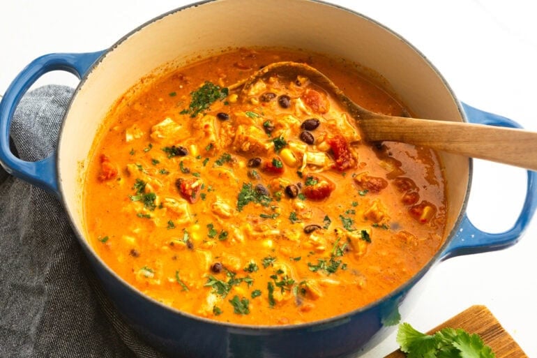 a wooden spoon stirring chicken enchilada soup in a large dutch oven pot