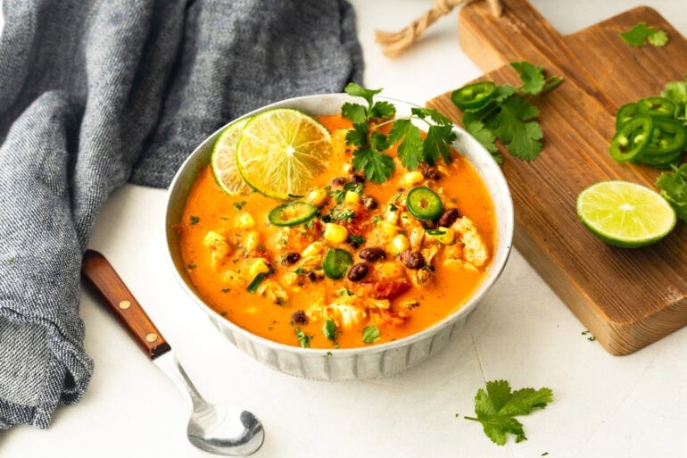 a soup bowl full of chicken enchilada soup topped with cilantro, jalapeno slices and lime slices