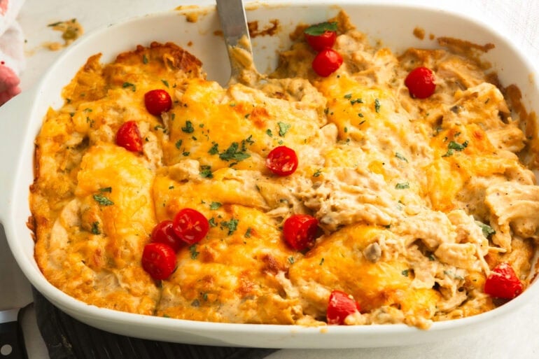 a casserole dish of chicken enchilada casserole that has been sliced into servings and a spatula about to lift a serving out of the pan