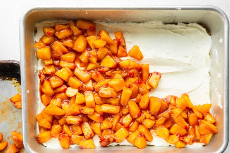a 9x13" baking dish with a creamy layer down being covered with juicy diced peaches