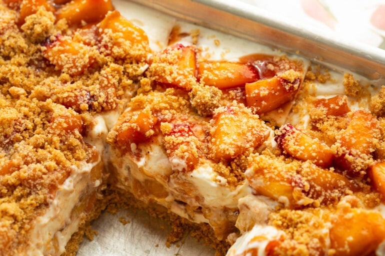 a layered creamy cheesecake and peach bars with one slice removed so you can see the layers
