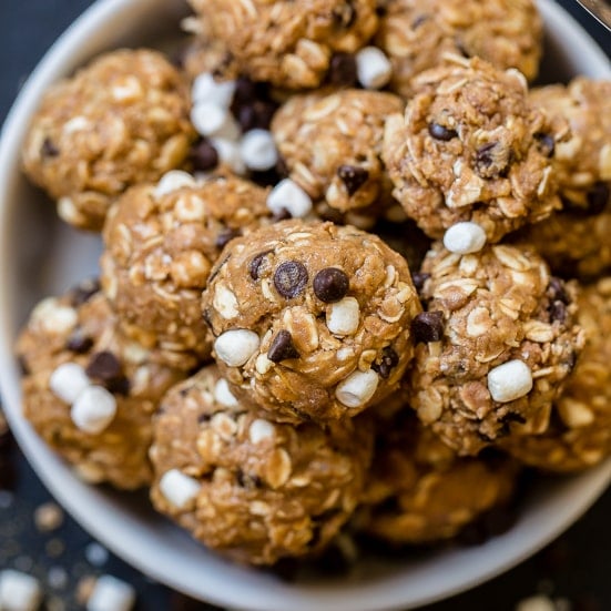 A black board with mini marshmallows, mini chocolate chips, and graham cracker crumbs sprinkled everywhere with protein no bake s'mores energy bites