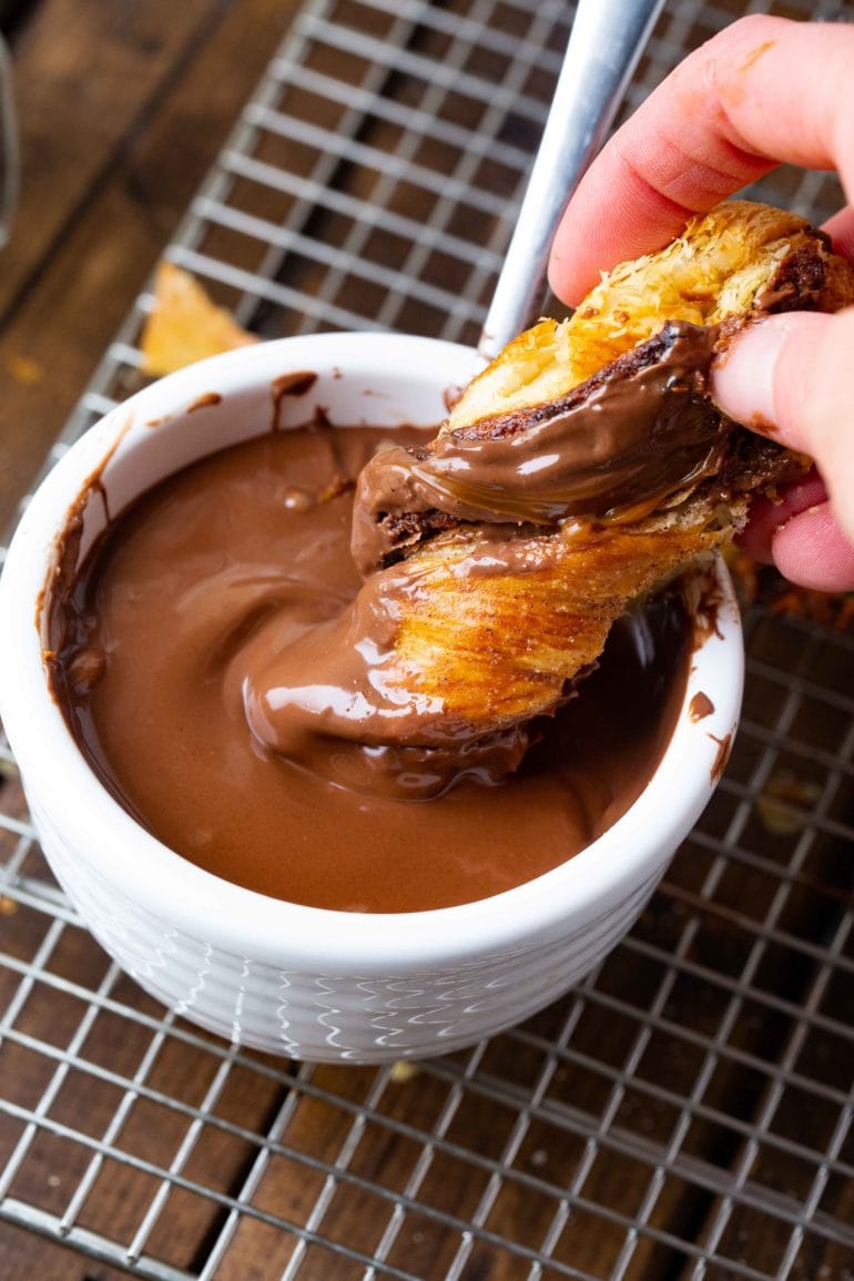 A photo of someone dipping a piece of a baked good into chocolate sauce