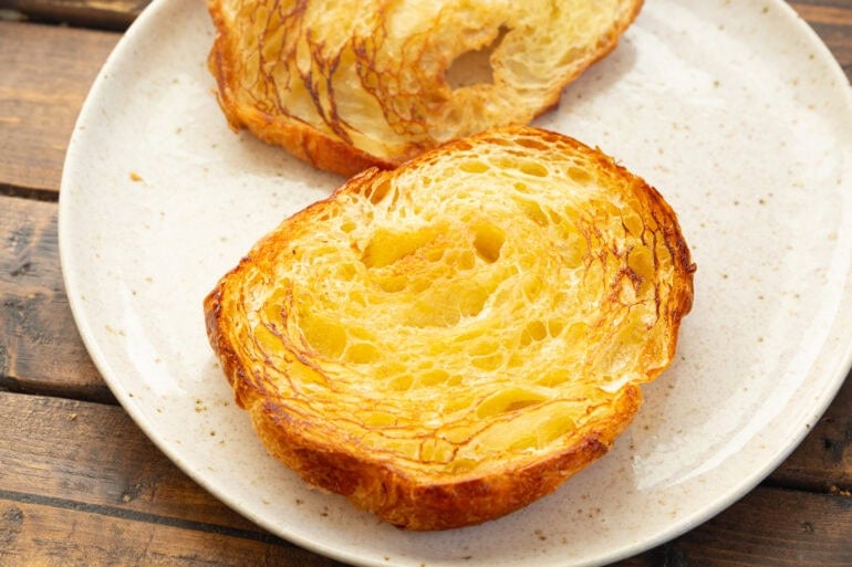 An open faced grilled flaky pastry sandwich sits on a white plate