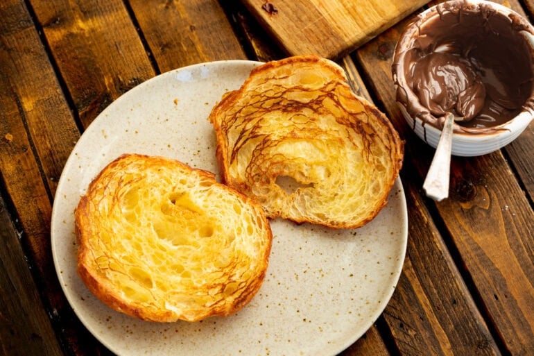 a grilled sliced croissant sits on a plate next to an open jar of nutella for strawberry nutella croissants
