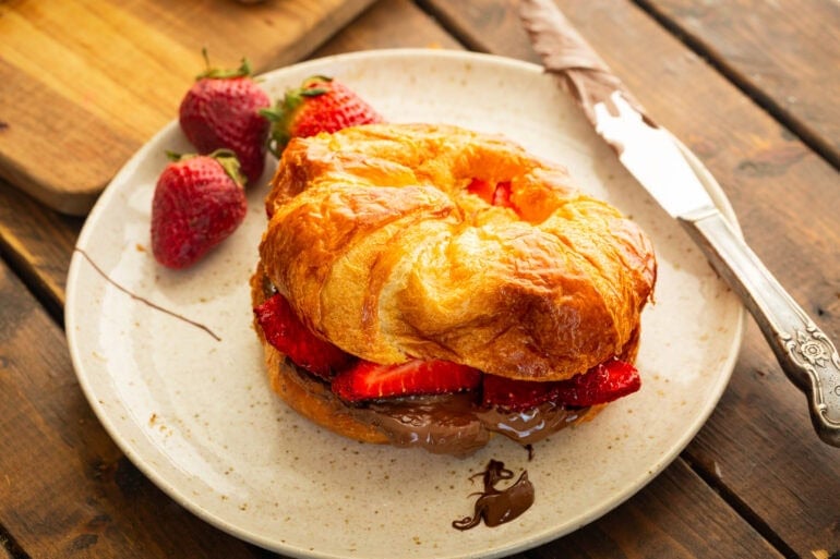 A flaky croissant sandwich with nutella, strawberries, and a grilled croissant with butter.