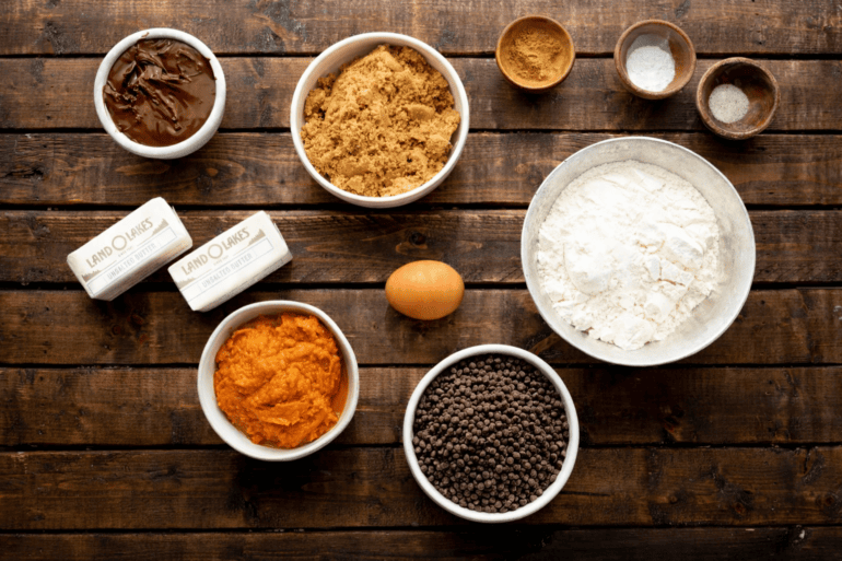 All the ingredients for pumpkin bars with browned butter including butter, nutella, brown sugar, flour, egg, pumpkin, chocolate chips, and spices.
