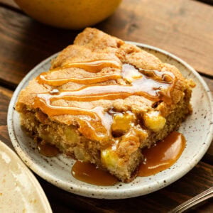 a slice of moist fresh apple cake on a small dessert plate topped with a drizzle of caramel sauce