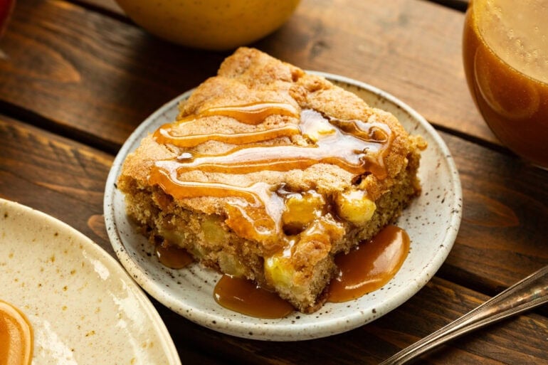 a slice of moist fresh apple cake on a small dessert plate topped with a drizzle of caramel sauce