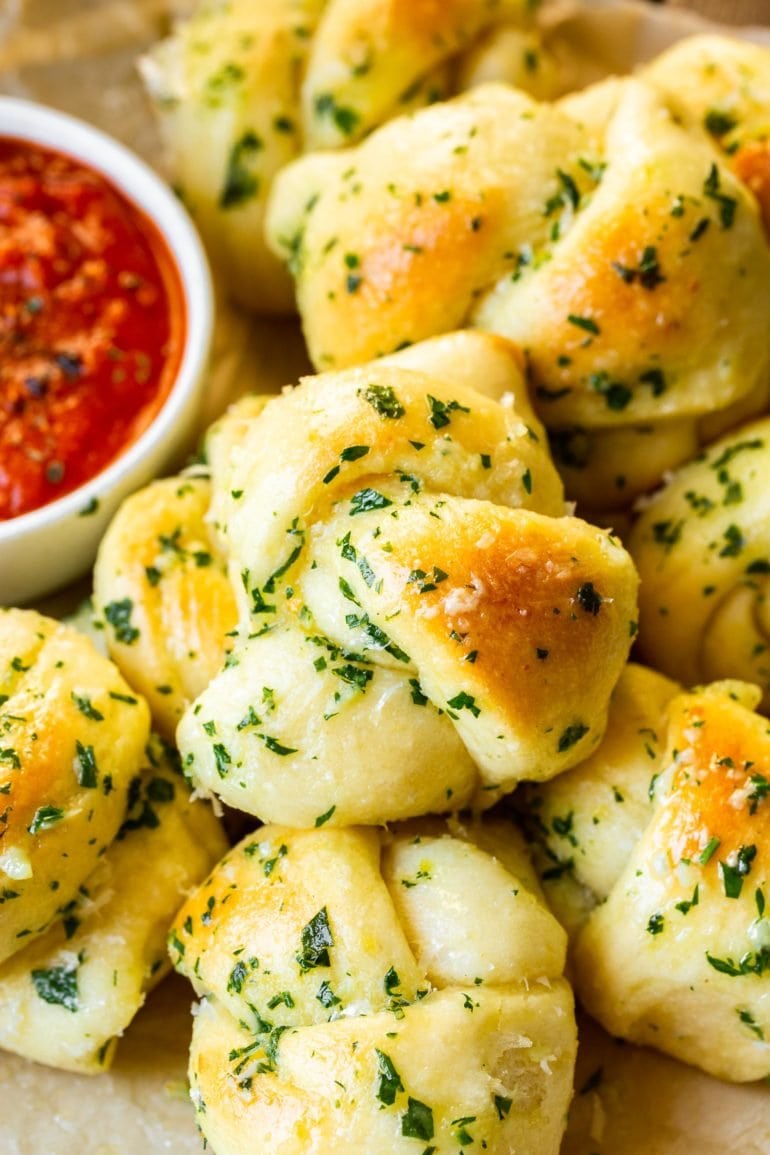 a photo of a perfectly golden buttery italian bread bites surrounded by more bread with a cup of pizza sauce on the side.