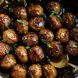 a large skillet full of browned meatballs in a sticky sauce and topped with chopped green onions and sesame seeds