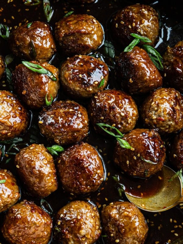 a large skillet full of browned meatballs in a sticky sauce and topped with chopped green onions and sesame seeds