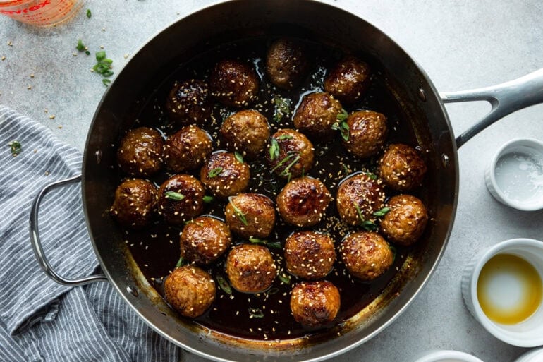 a large skillet full of saucy korean meatballs topped with sesame seeds and chopped green onions
