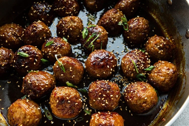 sweet and savory korean meatballs sitting in a sticky sauce with green onions and sesame seeds sprinkled over the top
