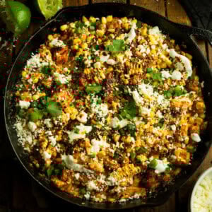 a photo of a cast iron skillet of cooked chicken chunks mixed with mexican street corn