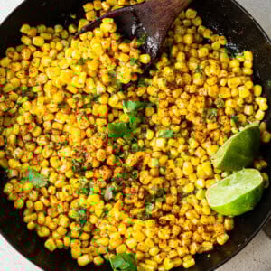 a cast iron skillet with charred corn, chopped cilantro, and lime wedges