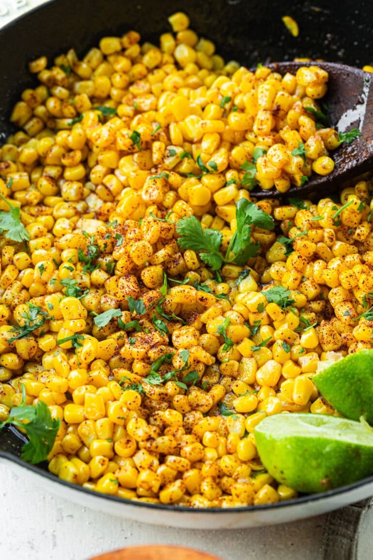 A serving spoon scooping honey butter skillet corn from the pan, with fresh chopped cilantro sprinkled on top.