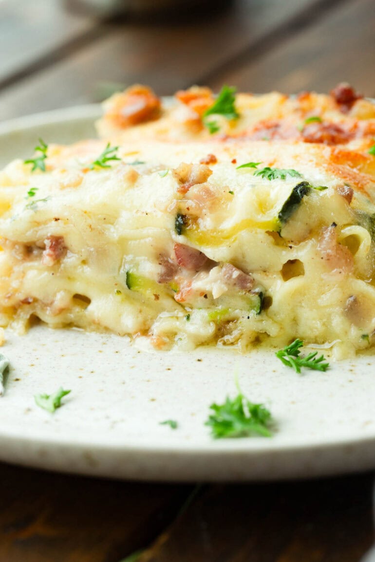 a photo of a piece of pancetta vegetable lasagna with white sauce sitting on a dinner plate