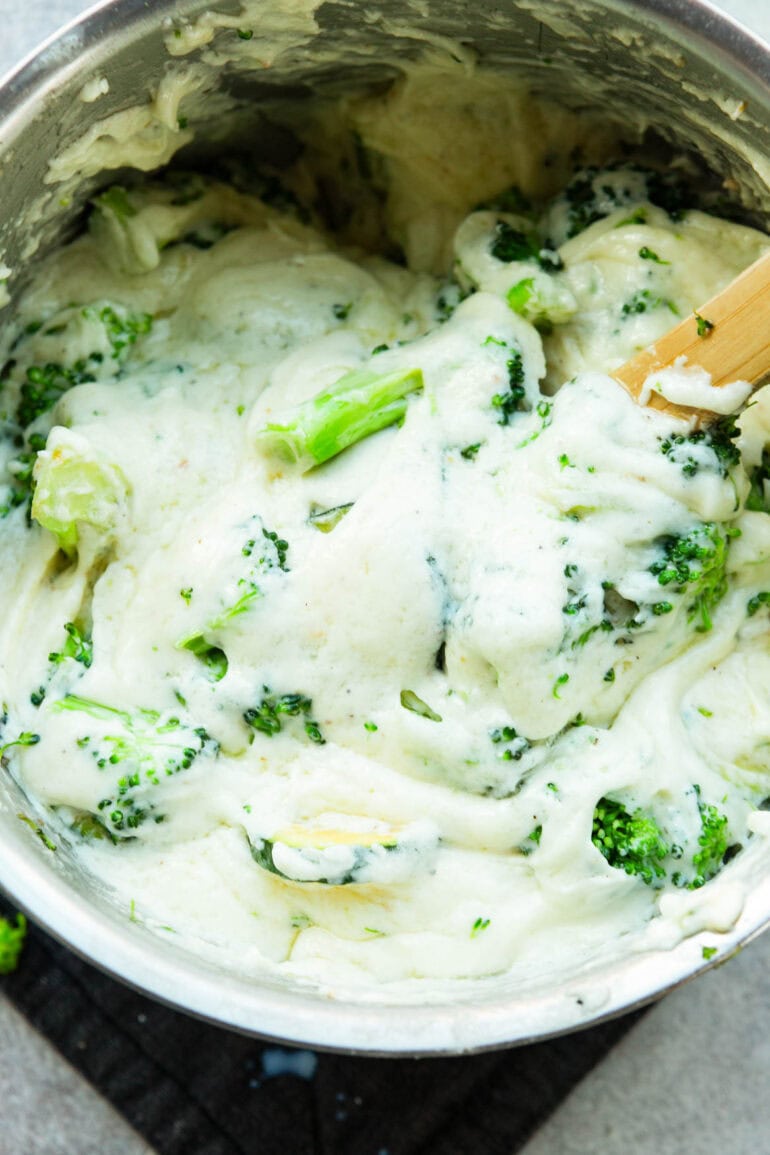 a photo of cooked broccoli and zucchini being stirred into a white bechamel sauce