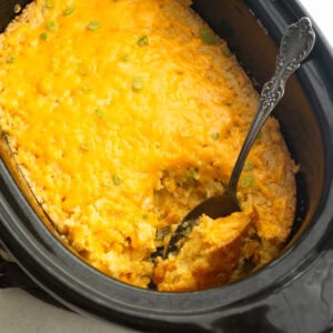 a crock pot full of corn casserole with a large serving spoon scooping up serving