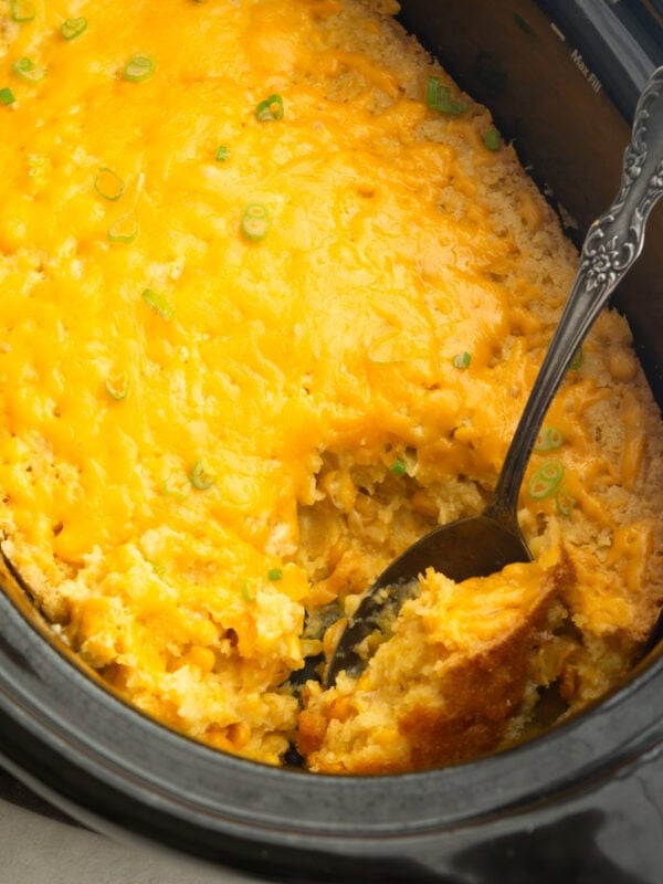 a crock pot full of corn casserole with a large serving spoon scooping up serving