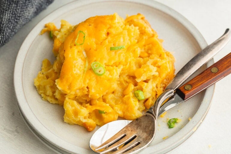 a serving of corn casserole on a dinner plate with a fork and spoon sitting next to it