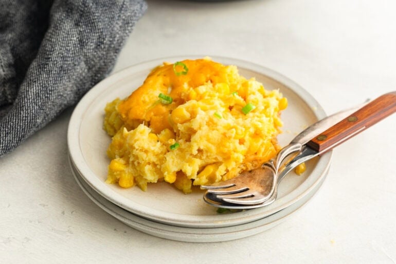 a serving of corn casserole on a dinner plate with a fork and spoon sitting next to it