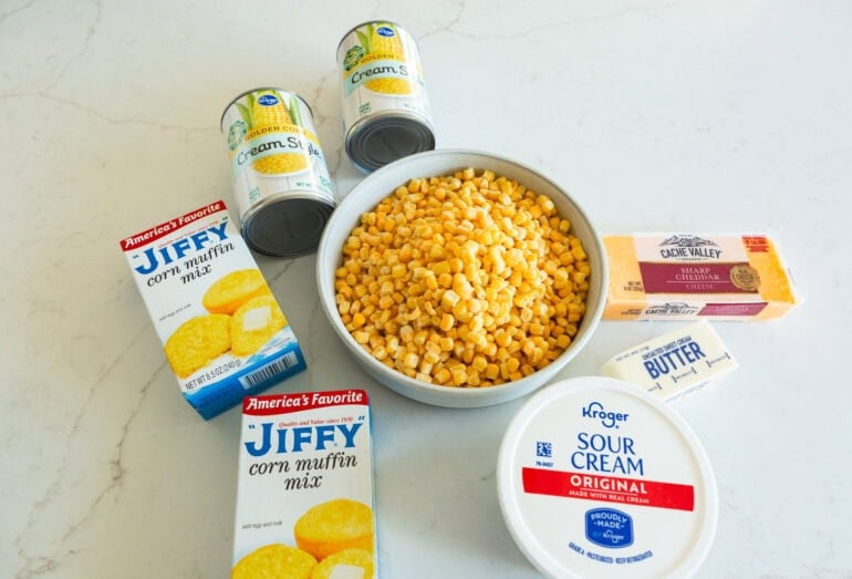 all the ingredients for corn casserole including fresh corn, canned cream corn, jiffy corn muffin mix, sour cream and cheese