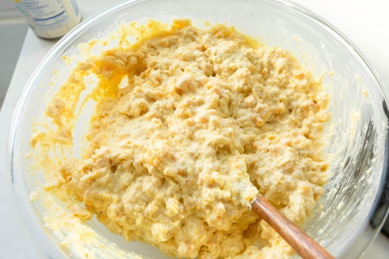 a wooden spoon stirring the batter for corn casserole in a large glass mixing bowl