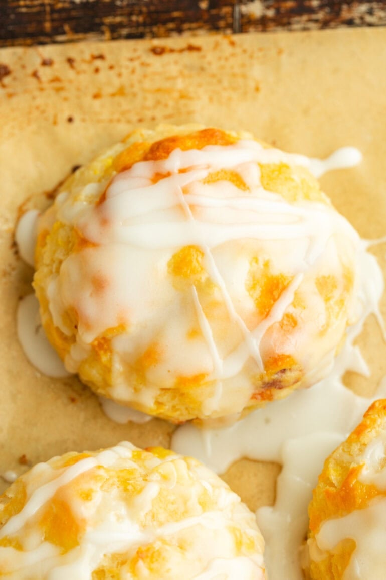 Golden brown biscuit with visible chunks of juicy peach and a smooth glaze dripping down the sides.