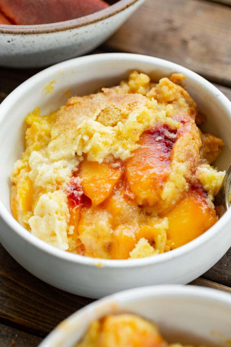a photo of a serving of juicy peach cobbler topped with a golden cake mix topping.
